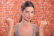 Young Woman Using Hand Weights In Front Of A Red Brick Wall